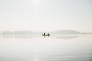 Two men in a canoe on vast calm water surface of the lake, sunny day - CAVF96282
