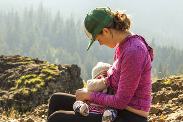 A young woman breast feeds an infant atop a mountain - CAVF96286