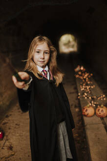 Girl with magic wand wearing witch costume standing in spooky tunnel - GMLF01300