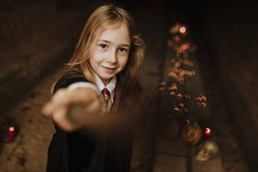 Blond girl with magic wand wearing witch costume standing in spooky tunnel - GMLF01301