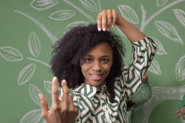 Woman with Afro hairstyle gesturing in front of green wall - EIF03965