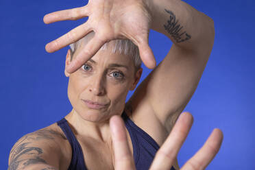 Frau mit kurzen Haaren gestikuliert vor blauem Hintergrund - EIF03998