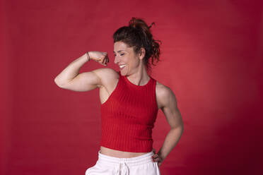 Lächelnde Frau, die Muskeln vor rotem Hintergrund anspannt - EIF04004