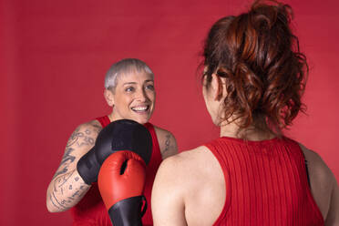 Glückliche Frau beim Boxen mit einem Freund vor rotem Hintergrund - EIF04013