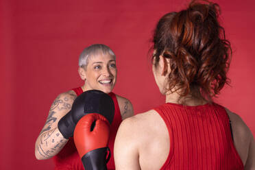 Happy woman boxing with friend against red background - EIF04013