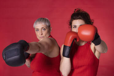 Friends wearing boxing gloves standing against red background - EIF04015