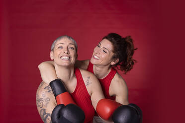 Happy friends with boxing gloves standing against red background - EIF04016