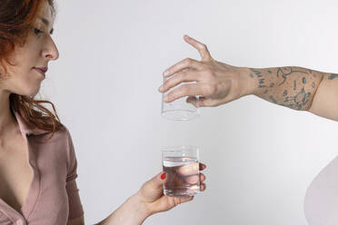 Hands of woman filling glass with water against white background - EIF04031
