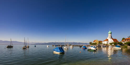 Deutschland, Bayern, Wasserburg am Bodensee, Klarer blauer Himmel über schwimmenden Booten im Bodensee mit der Kirche des Heiligen Georg im Hintergrund - WDF06928