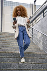 Businesswoman walking down on staircase using smart phone - VEGF05581