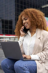 Lächelnde Geschäftsfrau mit Laptop, die mit einem Smartphone spricht - VEGF05584