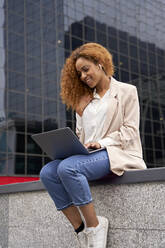 Junge Geschäftsfrau arbeitet an einem Laptop vor einem Bürogebäude - VEGF05590