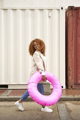 Smiling businesswoman walking with cpink inflatable ring - VEGF05596