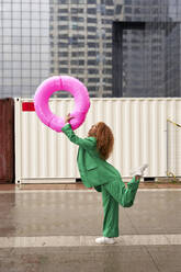Glückliche Geschäftsfrau spielt mit aufblasbarem Ring auf dem Gehweg - VEGF05602