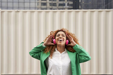 Happy businesswoman listening music through wireless headphones in front of wall - VEGF05607