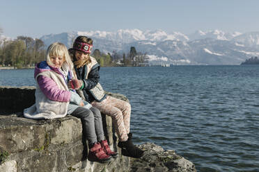 Happy sisters sitting on wall by lake - TYF00139