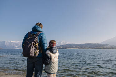 Father wearing backpack standing with daughter in front of lake - TYF00140