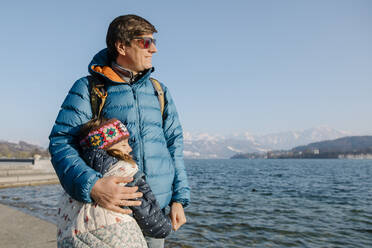 Happy father wearing sunglasses standing with daughter by lake on sunny day - TYF00141