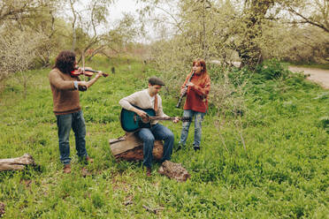 Mann übt Gitarre mit Freunden, die auf einem Feld Geige und Klarinette spielen - MRRF02016