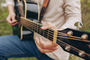 Männerhände zupfen an den Saiten einer Gitarre - MRRF02027