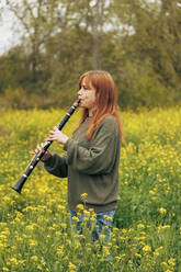 Redhead woman practicing clarinet standing in flower field - MRRF02041