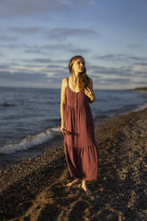 Woman holding flute standing at beach - SSGF00831