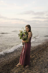 Frau hält Blumenstrauß am Strand - SSGF00840