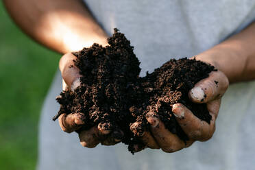 Closeup of two hands holding dark brown dirt on a sunny day - CAVF96299