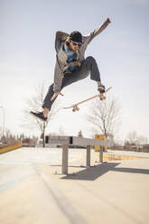 Young skateboard enthusiast in skatepark jumping over bench - CAVF96309