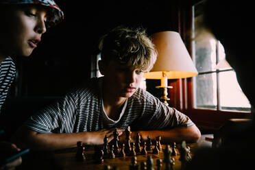 Boys Play Chess together in a rustic cabin by window light - CAVF96311