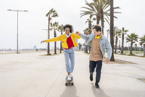 Glücklicher Mann bringt einer Frau auf dem Fußweg das Skateboardfahren bei - OIPF01587