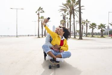 Lächelnde Frau mit Mann nimmt Selfie durch Handy auf Skateboard - OIPF01594