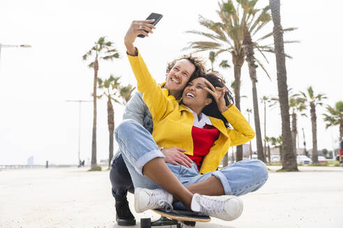 Glückliche Frau mit Mann nimmt Selfie durch Smartphone auf Skateboard - OIPF01595