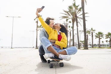 Man embracing woman taking selfie through mobile phone on footpath - OIPF01596