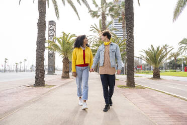 Happy couple holding hands walking in front of trees on footpath - OIPF01600