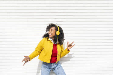 Happy woman wearing headphones dancing in front of white corrugated shutter - OIPF01610