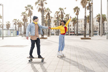 Smiling woman holding hands with man skating together on footpath - OIPF01631