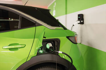 Green electric car being charged by wall at charging station - GMCF00283
