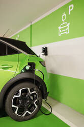 Green car being charged by wall at electric charging station - GMCF00284