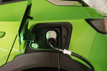 Green electric car being charged by plug at charging station - GMCF00288