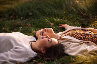 Happy lesbian couple smiling while lying on grass with eyes closed - CAVF96317