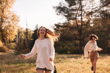 Zwei glückliche junge Frauen lächelnd beim Laufen im Wald im Herbst - CAVF96318