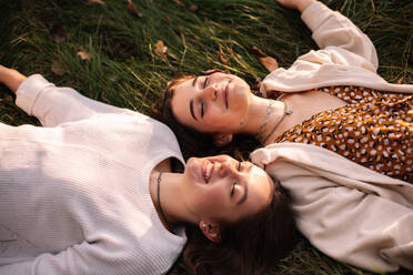 Two happy teenage girls smiling while lying on grass with eyes closed - CAVF96319