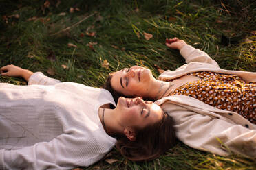 Two happy female friends smiling while lying on grass with eyes closed - CAVF96320