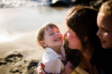 Mutter umarmt jungen Sohn am Strand in San Diego bei Sonnenuntergang - CAVF96366