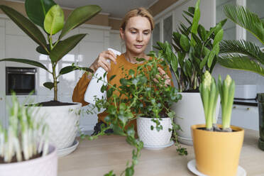 A nice woman in a yellow jacket is watering her home plants. - CAVF96386