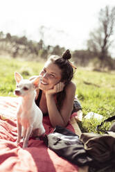 Schöne Frau mit Gesichtsbemalung und weißem kleinen Hund sitzen auf Gras - CAVF96397