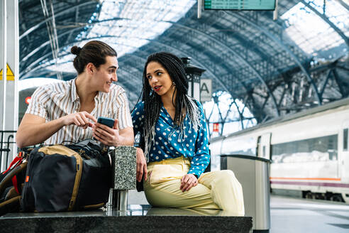 Unterschiedliches Paar beim Surfen auf dem Smartphone im Bahnhof - CAVF96468