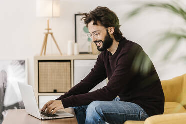 Glücklicher Mann mit Brille, der zu Hause einen Laptop benutzt - XLGF02907