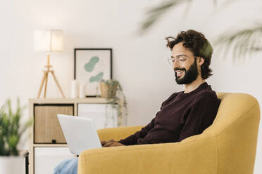 Lächelnder Mann mit Laptop auf dem Sofa zu Hause - XLGF02915